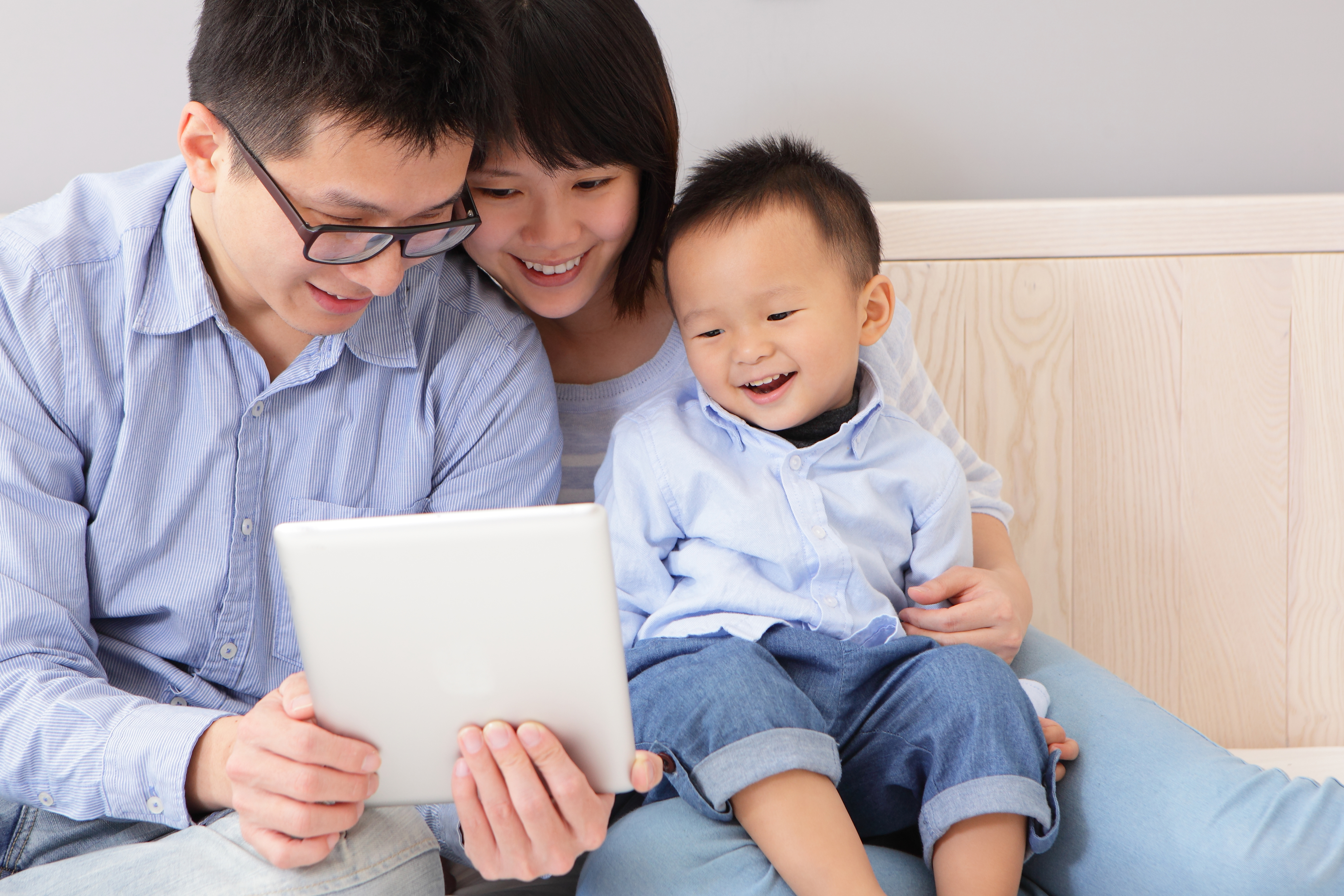 closeup of a happy, family of mother, father, son sitting on bed at home having fun using a tablet pc, asian people