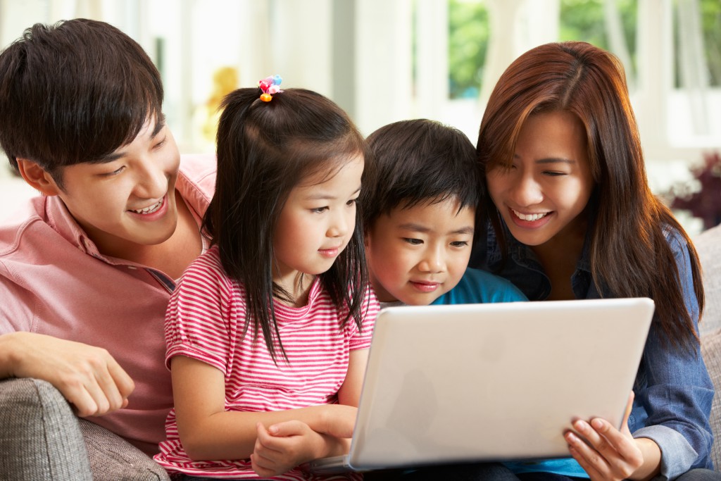 Chinese Family Using Laptop Whilst Relaxing On Sofa At Home