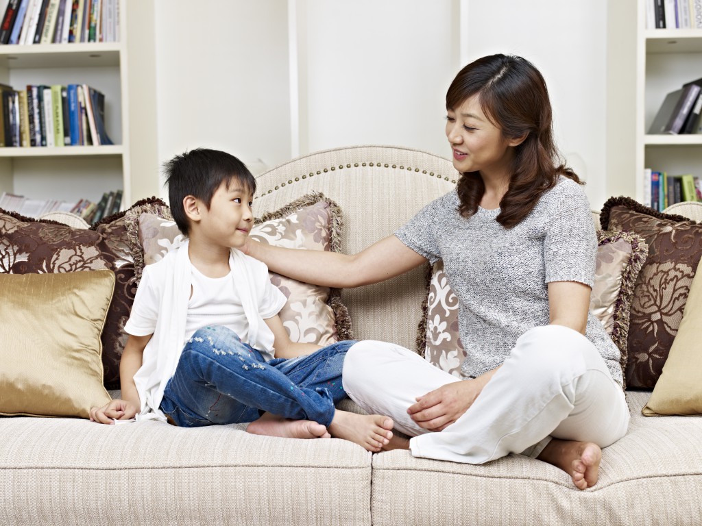 asian mother and son having a conversation on couch at home