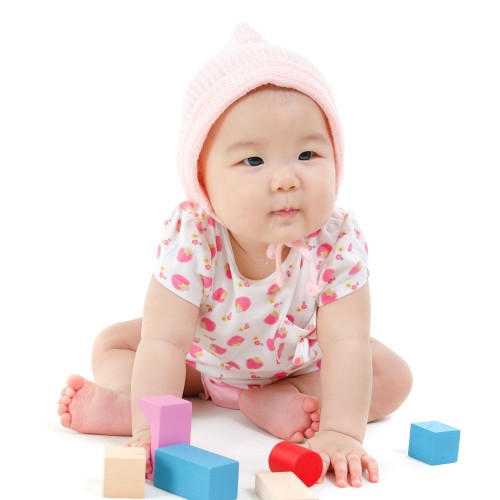 Adorable Asian baby girl playing wood blocks on floor, sitting isolated on white background.